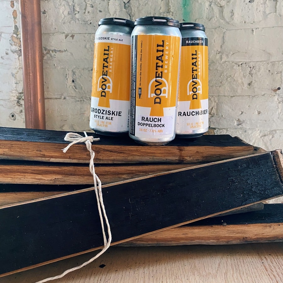 A picture of a 4-pack of Dovetail Rauchbier on top of a bundle of retired barrel staves